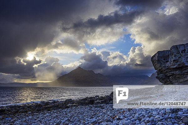 Schottische Küste mit Sonne  die durch die dramatischen Wolken über Loch Scavaig auf der Isle of Skye in Schottland  Vereinigtes Königreich  bricht