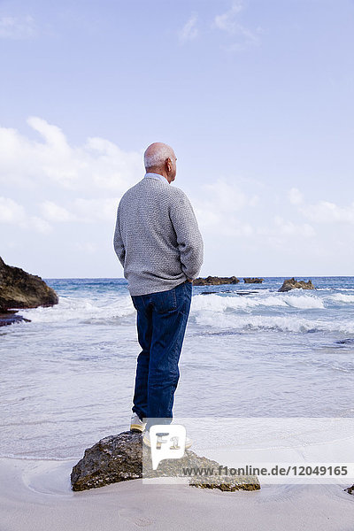 Mann steht auf einem Felsen und schaut aufs Meer hinaus