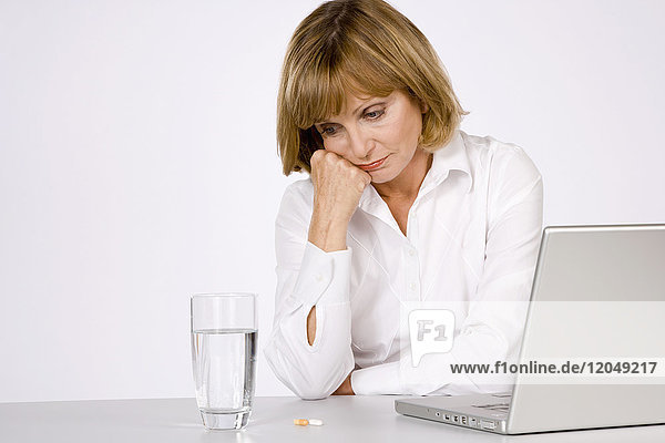 Frau mit Wasserglas  Pillen und Laptop-Computer