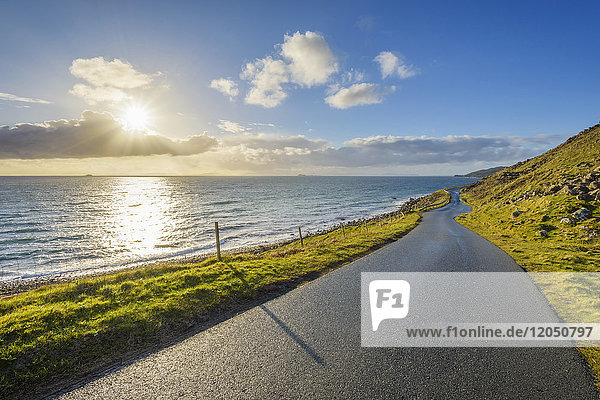 Typical Scottish landscape on the Isle of Skye with a coastal road and the sun shining over the ocean  Scotland  United Kingdom