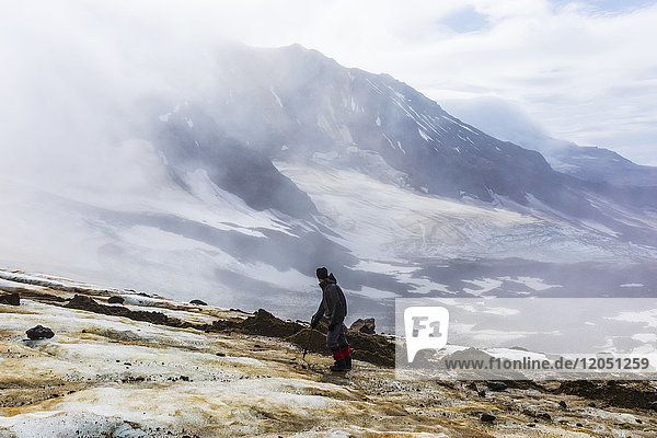 A man looks toward Trident Volcano through clouds while ascending the Knife Creek Glaciers in Katmai National Park; Alaska  United States of America