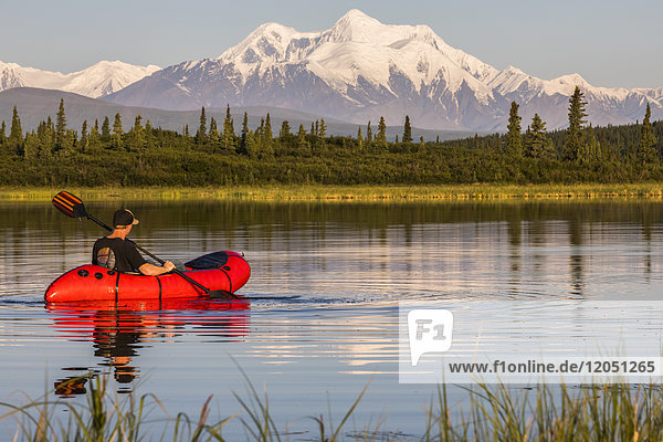A man paddles a pack raft across Donnelly Lake with Mt. Hayes towering in the distance; Alaska  United States of America