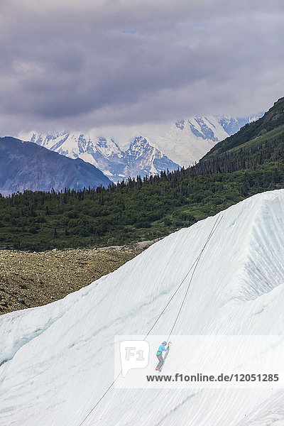 A woman ice climbs on Root Glacier in Wrangell-St. Elias National Park with Mt. Blackburn in the background; Alaska  United States of America