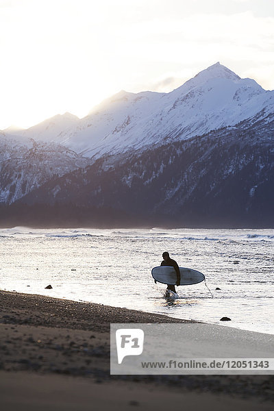 Surfer trägt sein Brett aus der Kachemak Bay  Homer Spit  Southcentral Alaska  USA