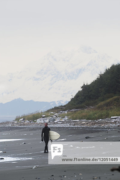 Surfer hält Surfbrett und geht am Ufer in der Nähe von Yakutat  Südost-Alaska  USA