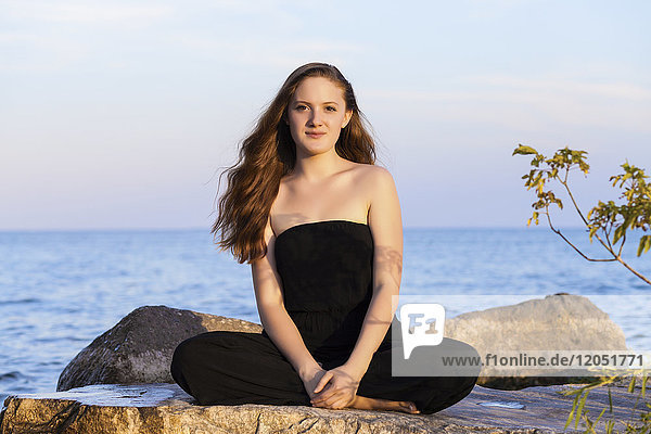 Portrait of a teenage girl sitting on rocks at Woodbine Beach in summer; Toronto  Ontario  Canada