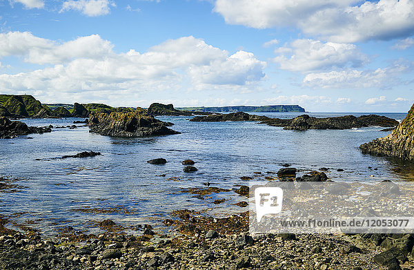 Rugged Coastline Of Northern Ireland With A Small Girl Sitting On The Rocks With A Net At The Water's Edge; Ireland