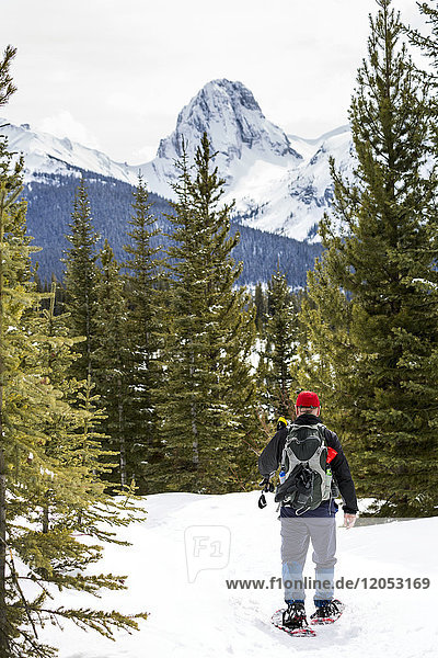 Männlicher Schneeschuhwanderer auf schneebedecktem Weg mit schneebedecktem Berg im Hintergrund; Alberta  Kanada