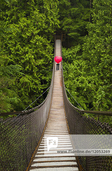 Frau mit einem roten  herzförmigen Regenschirm beim Überqueren der Lynn-Canyon-Hängebrücke  Nord-Vancouver; Vancouver  British Columbia  Kanada