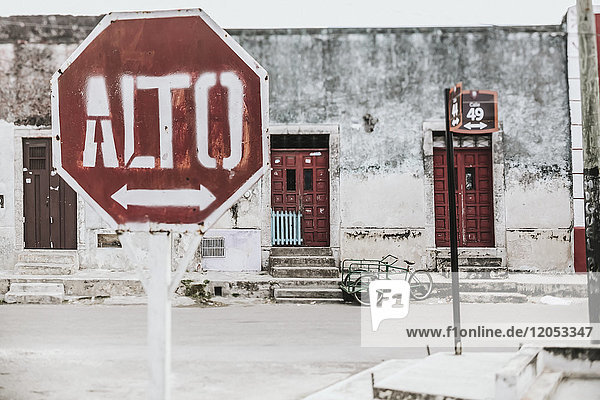 Ein Stoppschild mit einem Pfeil auf Spanisch entlang einer Straße mit Häusern im Hintergrund; Cancun,  Mexiko