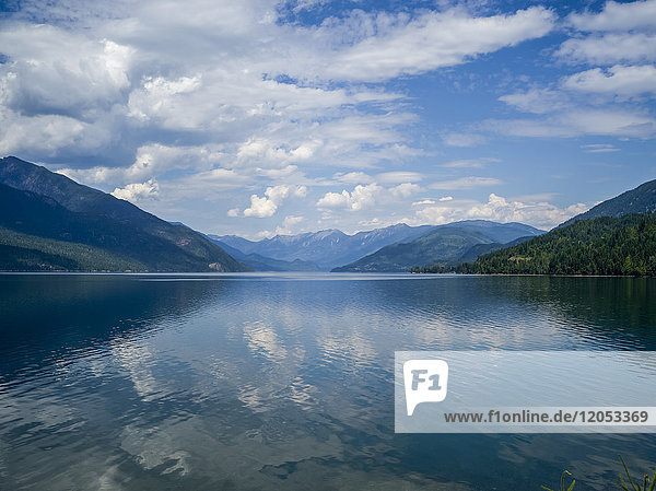 Der blaue Himmel und die Wolken spiegeln sich im ruhigen Wasser des Kootenay Lake in den Selkirk Mountains; Nelson  British Columbia  Kanada