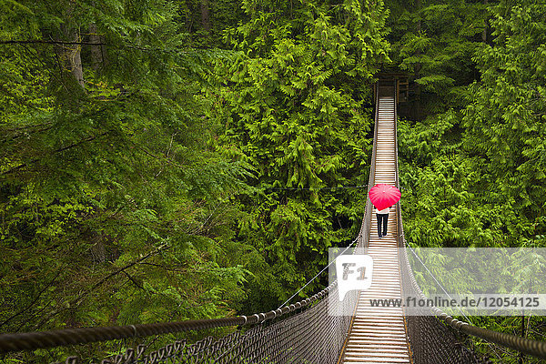 Frau mit einem roten  herzförmigen Regenschirm beim Überqueren der Lynn-Canyon-Hängebrücke  Nord-Vancouver; Vancouver  British Columbia  Kanada