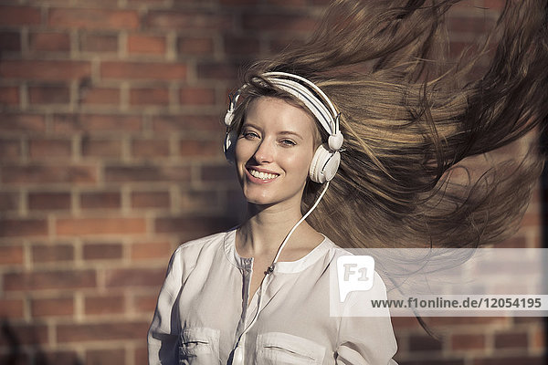 Porträt einer glücklichen Frau mit Kopfhörern und blasenden Haaren