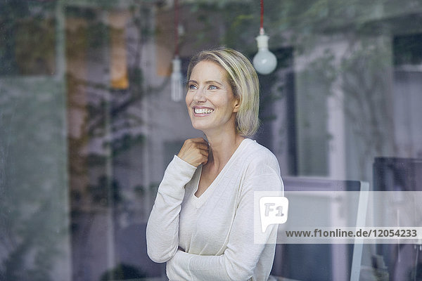 Porträt einer lachenden blonden Frau  die hinter einer Fensterscheibe steht