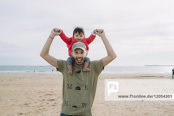 Porträt des Vaters  der seine kleine Tochter auf den Schultern am Strand trägt.