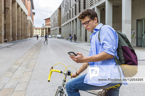 Young man on racing cycle looking at cell phone