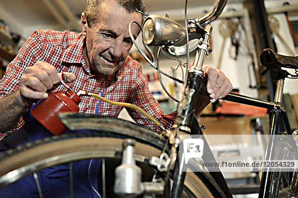 Senior Mann beim Ölen von Fahrrädern in seiner Werkstatt