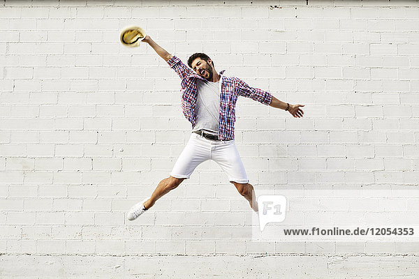 Happy man jumping mid-air in front of white wall