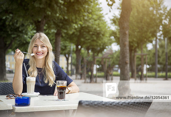 Porträt einer lachenden  blonden Frau  die auf dem Bürgersteig sitzt.