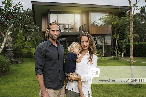 Porträt einer lächelnden Familie  die vor ihrem Designhaus steht  umgeben von einem üppigen tropischen Garten.