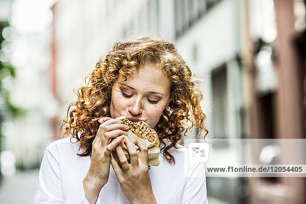 Porträt einer jungen Frau beim Bagelessen im Freien