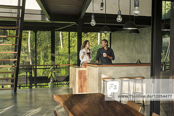 Paar beim Frühstücken und Lächeln in einer modernen Design-Küche mit Glasfassade  umgeben von einem üppigen tropischen Garten.