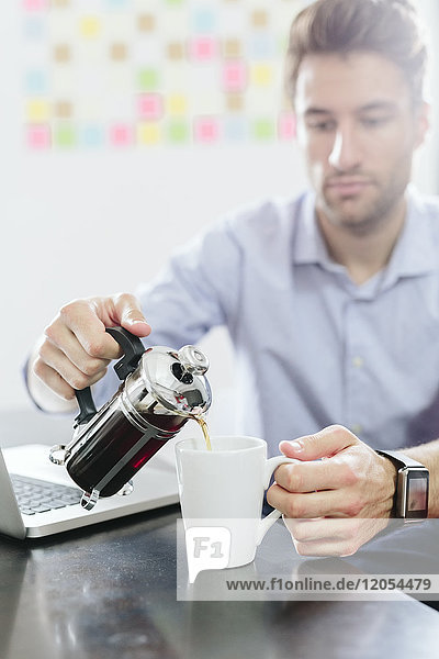 Young businessman sitting at desk with pot of coffee