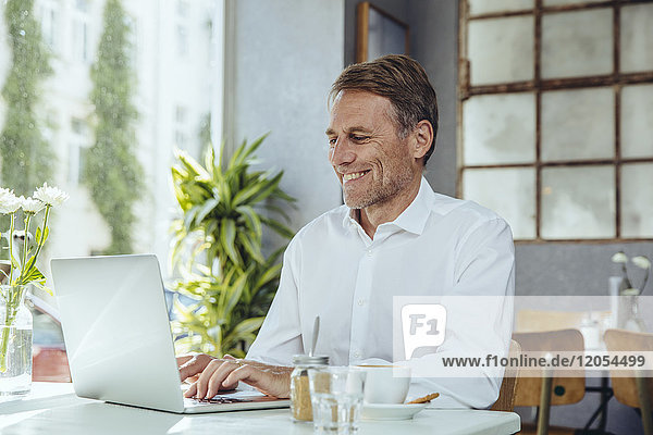Smiling businessman working in cafe with laptop
