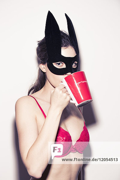 Junge Frau mit Dessous und Augenmaske  die aus der Tasse trinkt.