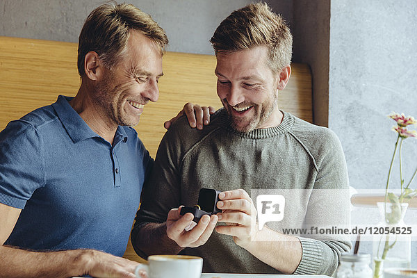 Excited gay couple with wedding ring in cafe