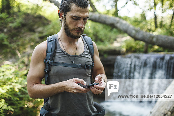 Young man holding cell phone at a waterfall in forest