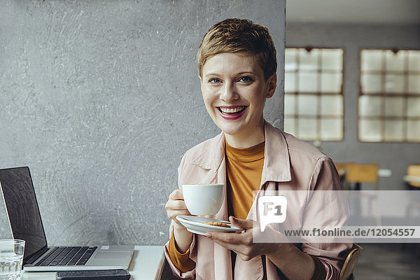 Porträt der lächelnden Frau im Café mit Laptop und Tasse Kaffee