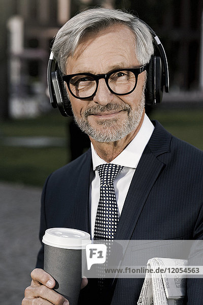 Grauhaariger Geschäftsmann mit Kopfhörer und Kaffee für den Blick in die Kamera