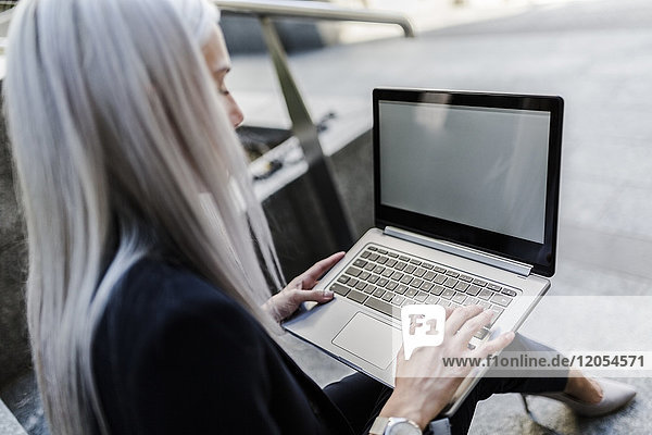 Young businesswoman sitting on stairs in the city using laptop
