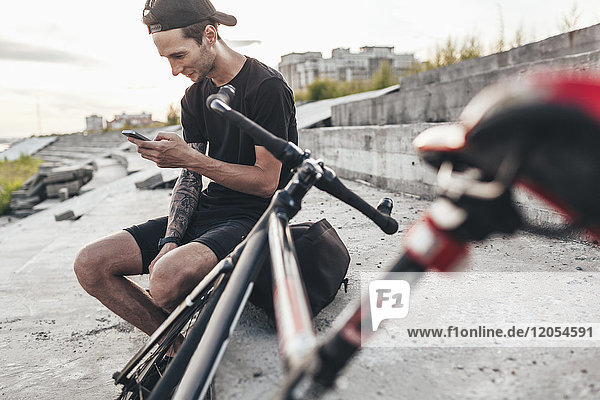 Junger Mann sitzt neben fixie bike mit Handy