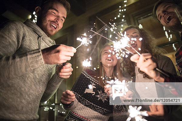 Happy friends holding sparklers outdoors at night