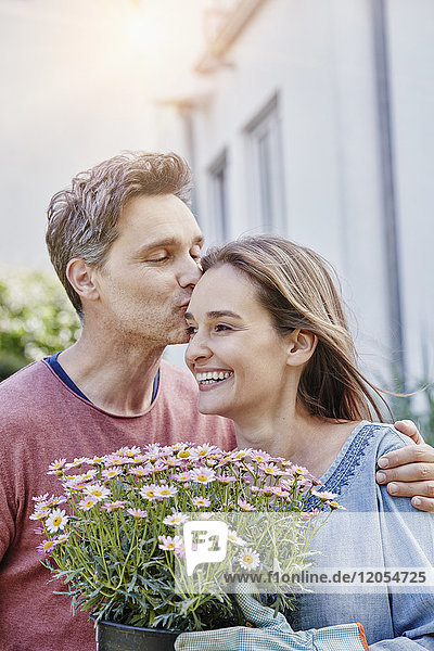 Mann küsst Frau mit Blumen vor ihrem Haus