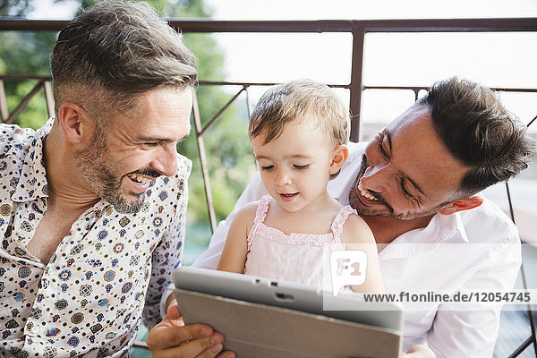 Glückliches schwules Paar mit Tochter auf dem Balkon mit digitalem Tablett