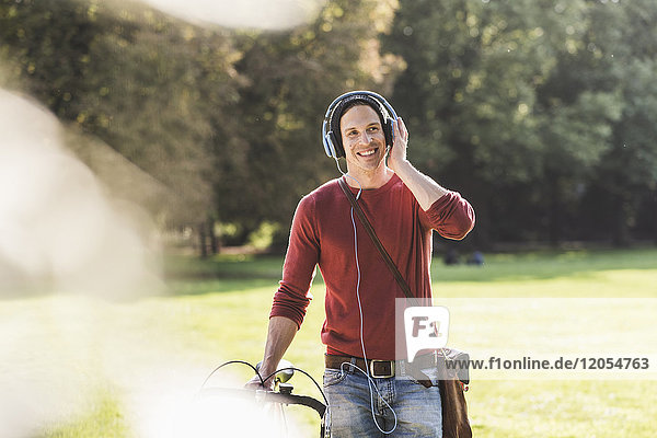 Laughing man with racing cycle listening music with headphones in a park