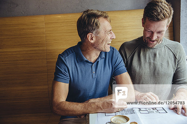 Happy gay couple looking at constructions plans for their home in cafe