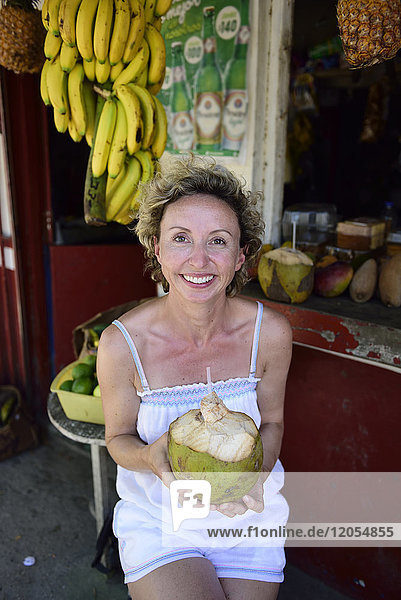 Portrait of smiling woman holding coconut in tropical fruit shop