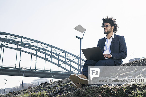 Businessman sitting at the riverside using laptop