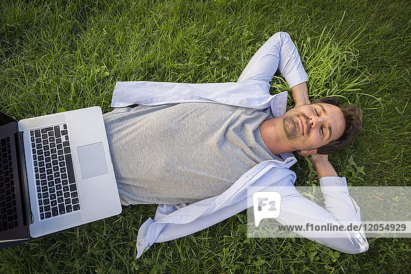 Mann entspannt sich im Sommer auf dem Rasen,  mit Laptop am Bauch
