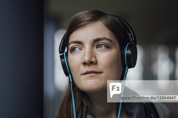 Portrait of daydreaming young woman listening music with headphones