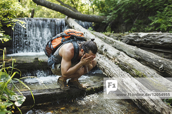 Junger Mann auf einer Wanderung erfrischend am Wasserfall