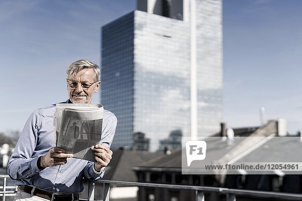 Grauhaariger Mann auf dem Balkon beim Zeitungslesen