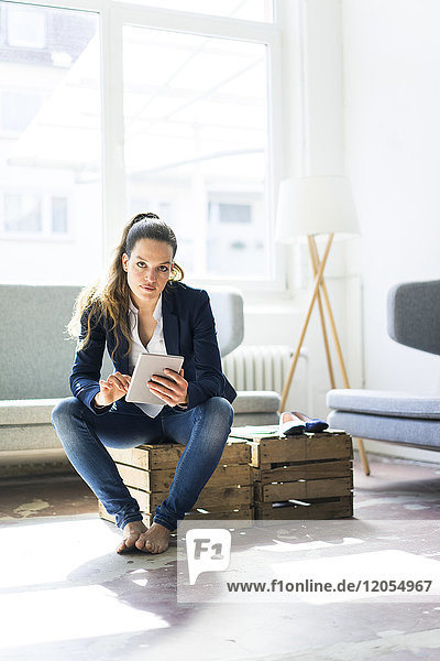 Businesswoman sitting on a crate using tablet