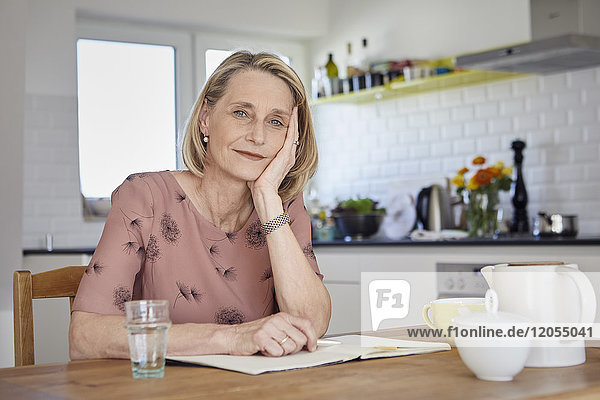 Porträt einer reifen Frau mit Notizbuch am Küchentisch