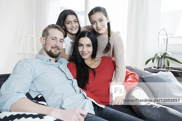 Familienporträt der Eltern und Zwillingstöchter auf Sofa im Wohnzimmer