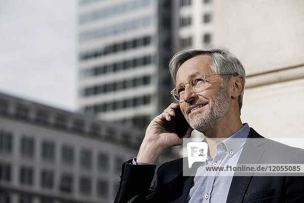 Grey-haired businessman on smartphone in the city
